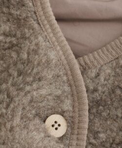 Søt vest fra HUTTEliHUT. Vesten har en fin V-hals som åpnes og lukkes foran med knapper. Perfekt å bruke som et lag over en genser for ekstra varme. Vesten er laget av 100% merinoull i teddy-tekstur med fôr, noe som sikrer en varm og komfortabel passform. Ved vask bruk et skånsomt ullvaskemiddel. Ikke bruk tøymykner. Velg alltid skånsom ullvask i maskin, og vreng plagget. Bruk et lavt sentrifugeringsprogram. Form plagget når det er vått. For håndvask, bruk lunkent vann og unngå å vri det opp. Trykk forsiktig med et håndkle for å fjerne overflødig vann. Legg flatt på et håndkle for å tørke – ikke legg på en radiator eller i en tørketrommel.