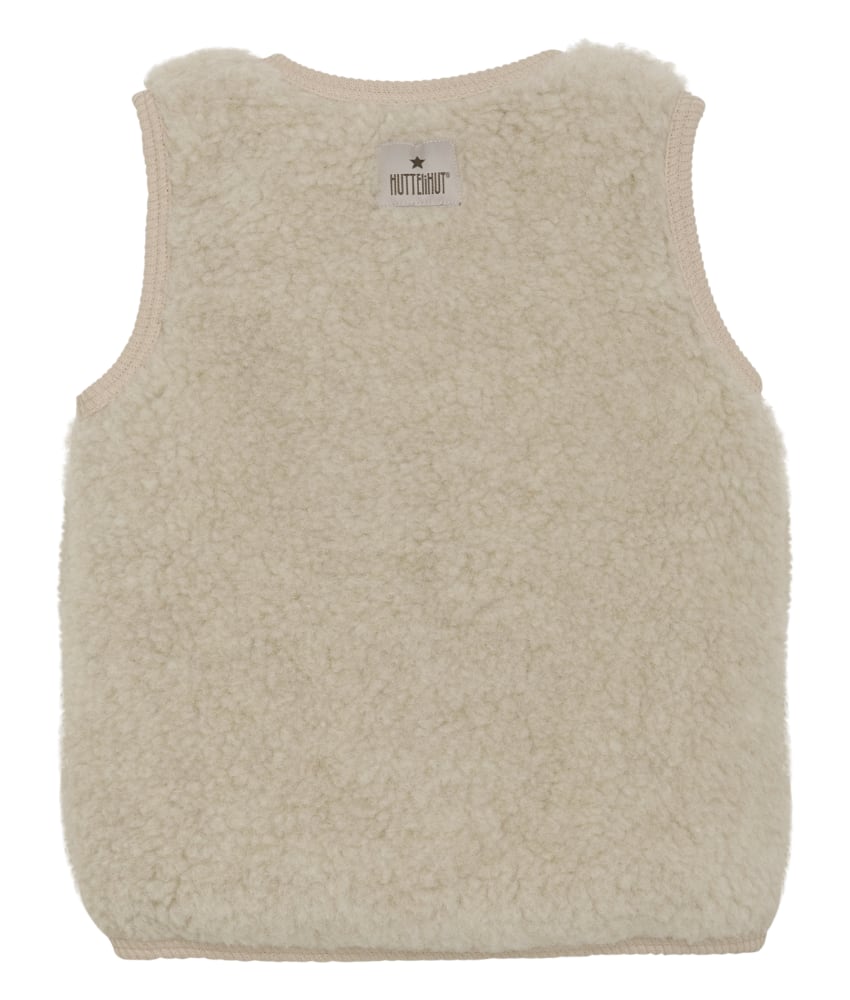 Søt vest fra HUTTEliHUT. Vesten har en fin V-hals som åpnes og lukkes foran med knapper. Perfekt å bruke som et lag over en genser for ekstra varme. Vesten er laget av 100% merinoull i teddy-tekstur med fôr, noe som sikrer en varm og komfortabel passform. Ved vask bruk et skånsomt ullvaskemiddel. Ikke bruk tøymykner. Velg alltid skånsom ullvask i maskin, og vreng plagget. Bruk et lavt sentrifugeringsprogram. Form plagget når det er vått. For håndvask, bruk lunkent vann og unngå å vri det opp. Trykk forsiktig med et håndkle for å fjerne overflødig vann. Legg flatt på et håndkle for å tørke – ikke legg på en radiator eller i en tørketrommel.