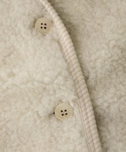 Søt vest fra HUTTEliHUT. Vesten har en fin V-hals som åpnes og lukkes foran med knapper. Perfekt å bruke som et lag over en genser for ekstra varme. Vesten er laget av 100% merinoull i teddy-tekstur med fôr, noe som sikrer en varm og komfortabel passform. Ved vask bruk et skånsomt ullvaskemiddel. Ikke bruk tøymykner. Velg alltid skånsom ullvask i maskin, og vreng plagget. Bruk et lavt sentrifugeringsprogram. Form plagget når det er vått. For håndvask, bruk lunkent vann og unngå å vri det opp. Trykk forsiktig med et håndkle for å fjerne overflødig vann. Legg flatt på et håndkle for å tørke – ikke legg på en radiator eller i en tørketrommel.