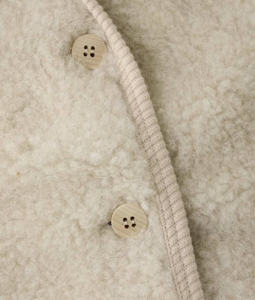 Søt vest fra HUTTEliHUT. Vesten har en fin V-hals som åpnes og lukkes foran med knapper. Perfekt å bruke som et lag over en genser for ekstra varme. Vesten er laget av 100% merinoull i teddy-tekstur med fôr, noe som sikrer en varm og komfortabel passform. Ved vask bruk et skånsomt ullvaskemiddel. Ikke bruk tøymykner. Velg alltid skånsom ullvask i maskin, og vreng plagget. Bruk et lavt sentrifugeringsprogram. Form plagget når det er vått. For håndvask, bruk lunkent vann og unngå å vri det opp. Trykk forsiktig med et håndkle for å fjerne overflødig vann. Legg flatt på et håndkle for å tørke – ikke legg på en radiator eller i en tørketrommel.