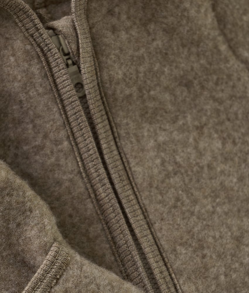 Smart og varm HUTTEliHUT dress i ullfleece. HUTTEliHUT dressen har en fast hette med en rund hodeform med små søte ører. Den har lange ermer og ben med praktiske folder opp til størrelse 80 for å holde små føtter og hender varme. Den har ribbekanter i alle åpninger. Den åpnes foran med en skjult glidelås med hakebeskyttelse. Laget av 100% merinoull. Dette produktet er kjent for sin holdbarhet hvis det behandles riktig: Vask det kun når det er nødvendig. Velg et skånsomt ullvaskemiddel. Ikke bruk tøymykner. Velg alltid skånsom ullvask i maskin, og vreng plagget på vrangen. Bruk et lavt sentrifugeringsprogram. Form plagget mens det er vått. Bruk lunkent vann til håndvask, og unngå å vri det opp. Trykk forsiktig med et håndkle for å fjerne overflødig vann. Legg flatt på et håndkle for å tørke – ikke legg på en radiator eller i en tørketrommel.