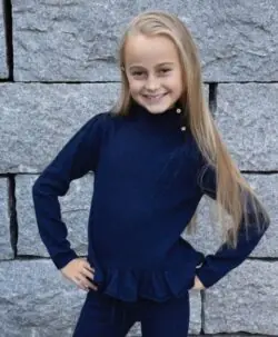 Marineblå strikket ullgenser fra Vilje & Ve med høy hals og knappedetaljer, komplettert med en sjarmerende rysjekant nederst. Perfekt for en varm og stilig look og er superfin til Aspen strikket bukse. Laget av 100% superfin merinoull. 